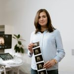 Expectant mother showing ultrasound images in a modern healthcare clinic setting.